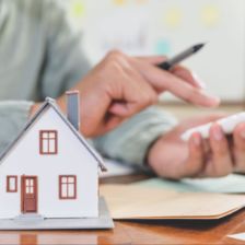 Man using a calculator next to a mini A-frame house & coin stack