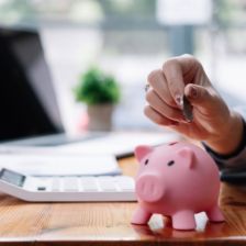 Woman putting coins into a piggy bank on her desk